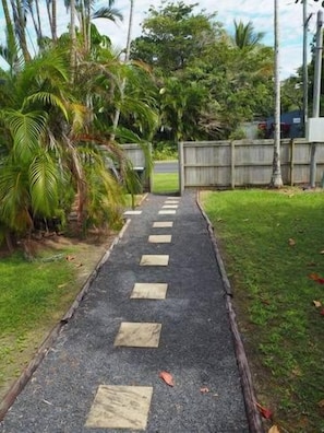 Pathway leads to a gated entrance surrounded by lush greenery and palm trees.