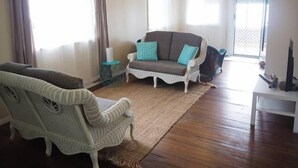 A living room with a white sofa, a wicker chair, and a small side table. - Feather Reef Cottage (Flying Fish Point)