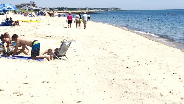 A beach with people sunbathing and walking along the shore.