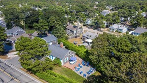 A residential area with houses surrounded by dense trees, a clear sky, and a road in the foreground.