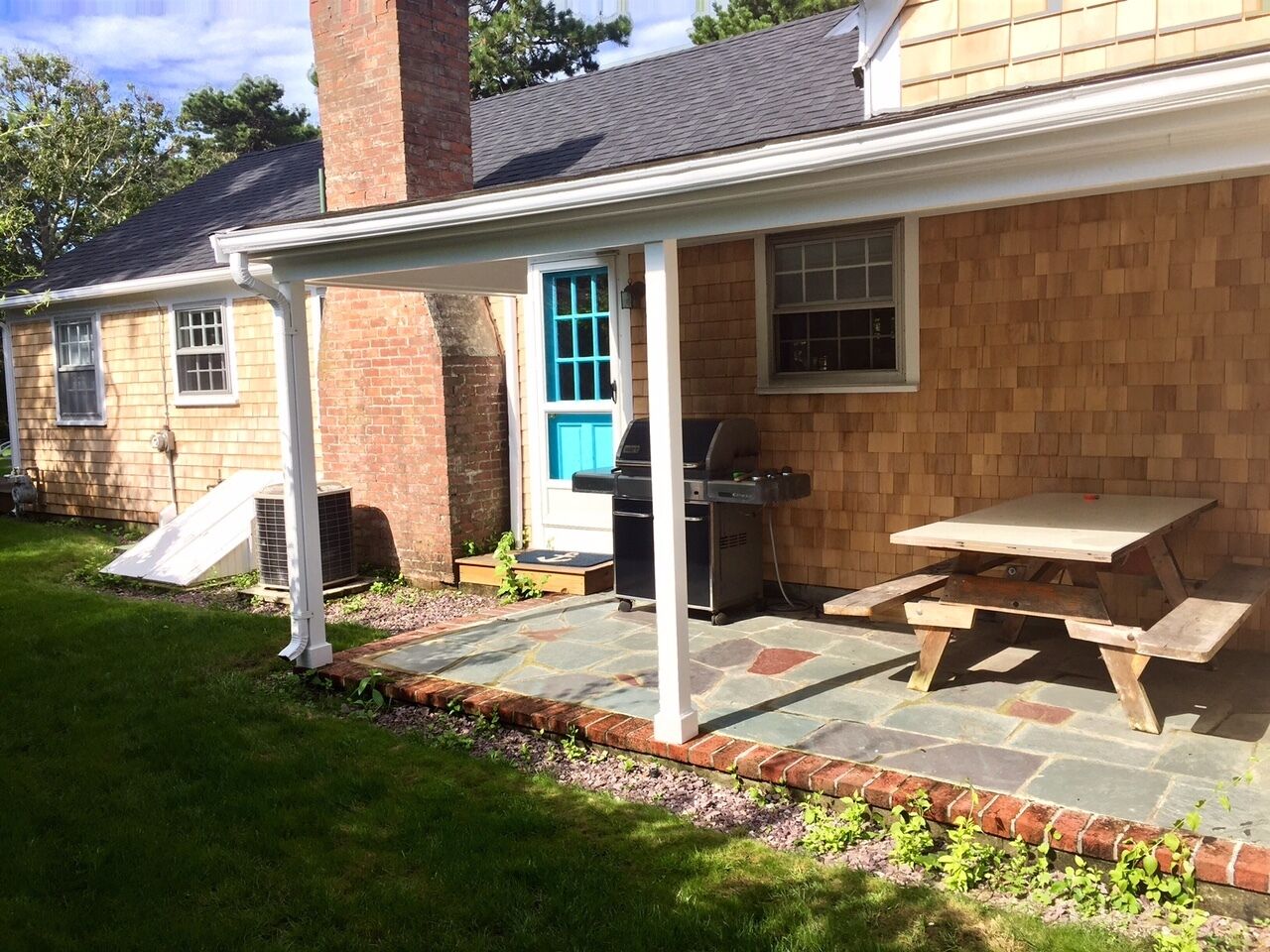 A backyard with a covered patio, a barbecue grill, and a picnic table.