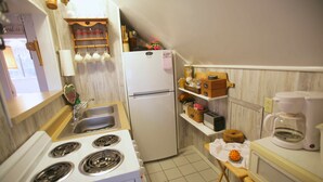 Une cuisine compacte équipée d’une cuisinière, d’un évier, d’un réfrigérateur et d’étagères contenant divers ustensiles de cuisine.