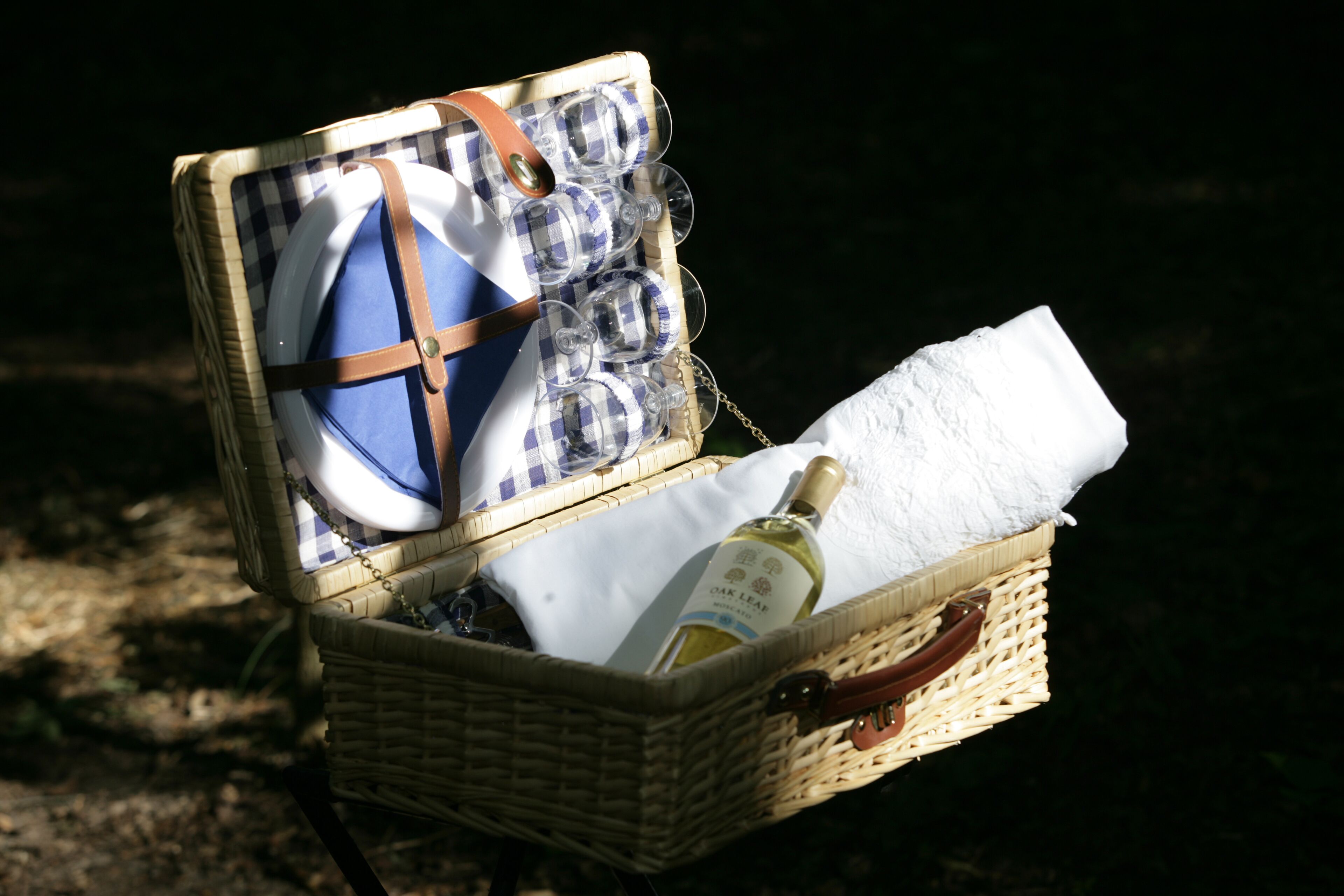 Un panier en osier contenant une bouteille de vin, un linge blanc plié et plusieurs verres à vin.