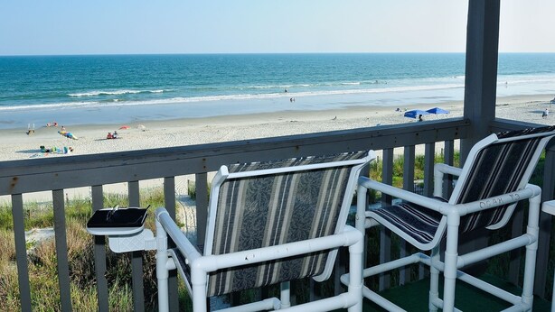 Une vue sur la plage depuis un espace abrité, équipé de chaises et d’une petite table.