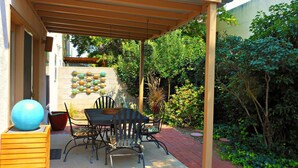 Ein überdachter Patio-Bereich mit Tisch und Stühlen, umgeben von Grünpflanzen und einer Zierwand.