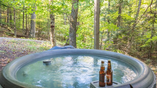 Un bain à remous situé dans une zone boisée, avec deux bouteilles de bière à proximité.