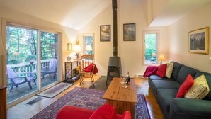 Un salon chaleureux avec une cheminée, un canapé, une table basse et une vue sur l’extérieur grâce à de grandes fenêtres.