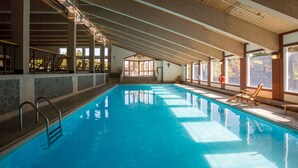Une piscine intérieure à l’eau d’un bleu cristallin, avec des poutres en bois au plafond et une bouée de sauvetage placée au bord du bassin.