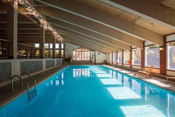 An indoor swimming pool with clear blue water, wooden beams on the ceiling, and a lifebuoy by the poolside.
