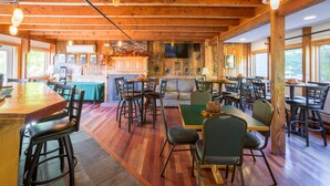Un grand espace dédié à la salle à manger, avec des tables et des chaises en bois, un coin bar et un téléviseur fixé au mur.