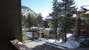 Ein verschneiter Bergblick mit einer Stegbrücke, schneebedeckten Bäumen und einem Gebäude mit einem verschneiten Dach.