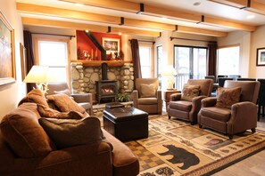 A cozy living room with a stone fireplace, leather sofas, and a patterned rug. - Premier 4 Bed, 4 Bath, by Village Gondola, Sleeps 10. New hot tub, sauna, pool. (Mammoth Lakes)