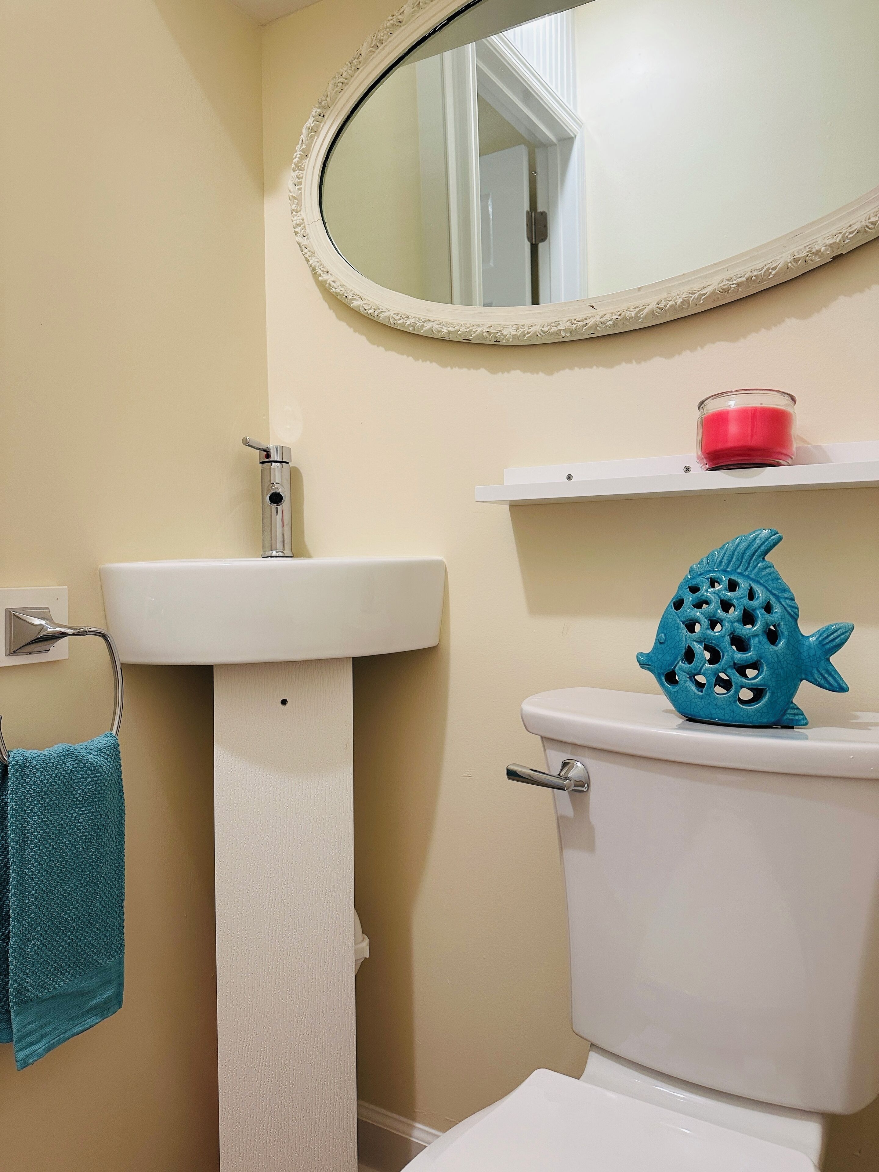 A bathroom with a white sink, a toilet, a blue fish-shaped soap dish, a towel rack with a blue towel, and a mirror with a decorative frame.