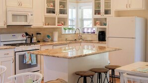 A modern kitchen with white cabinets, a central island, a microwave, stove, and a refrigerator. - The Cottage, A Tranquil Pet-Friendly Retreat on 42 Acres at Lost Pines Shire (Paige)