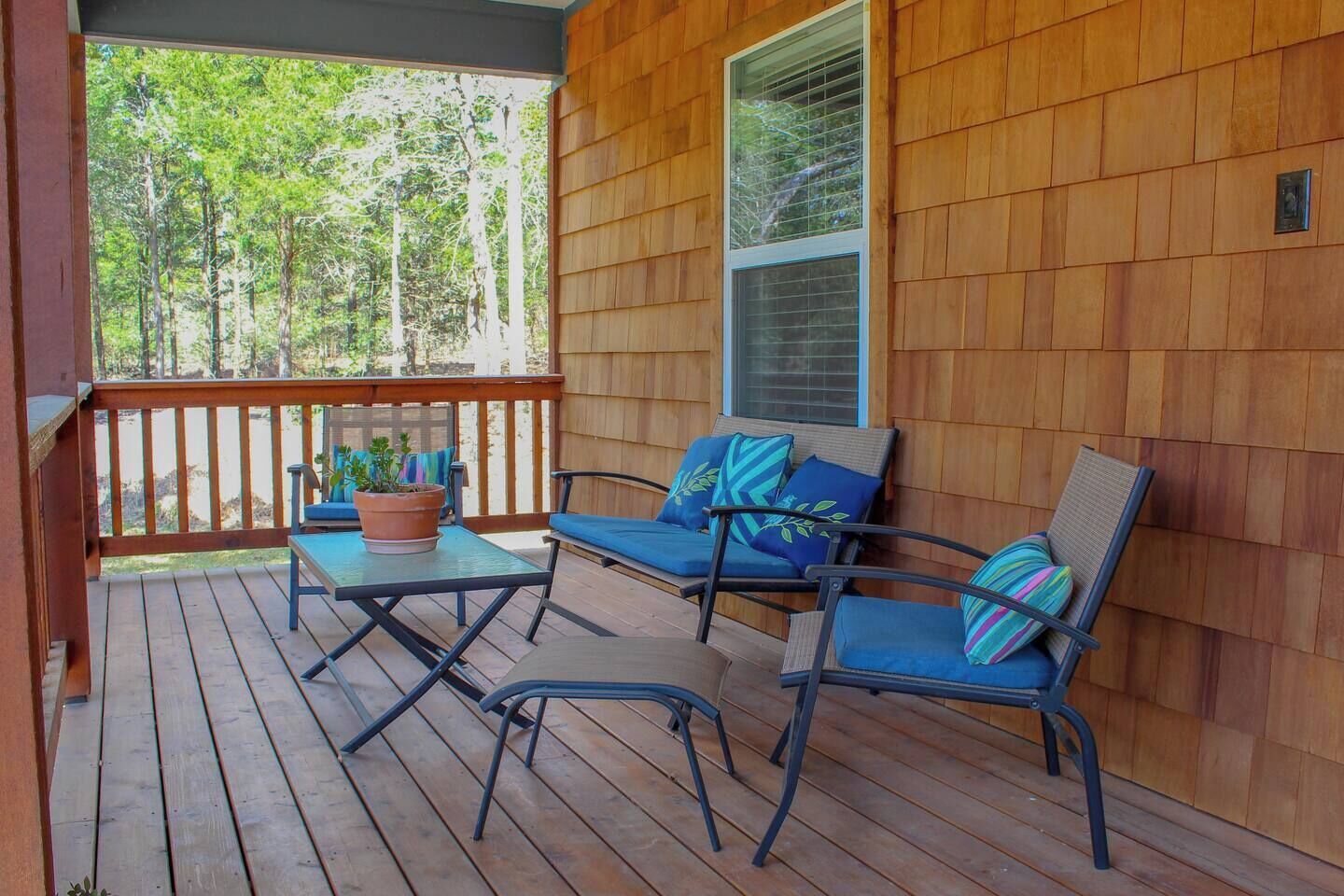 Une terrasse en bois avec une table et deux chaises, une plante en pot et une fenêtre.