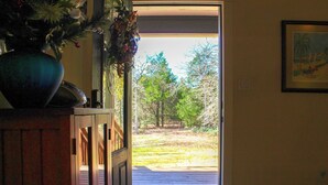 A doorway leading to a wooden deck with a view of a forested area. - The Cottage, A Tranquil Pet-Friendly Retreat on 42 Acres at Lost Pines Shire (Paige)