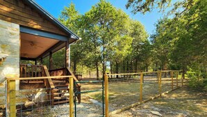 A covered outdoor area with a wooden deck, a fenced enclosure, and a gravel ground. - The Cottage, A Tranquil Pet-Friendly Retreat on 42 Acres at Lost Pines Shire (Paige)