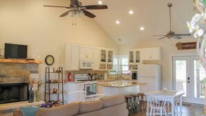 A spacious living room with a fireplace, a dining area, and a kitchen with white cabinets and a central island. - The Cottage, A Tranquil Pet-Friendly Retreat on 42 Acres at Lost Pines Shire (Paige)