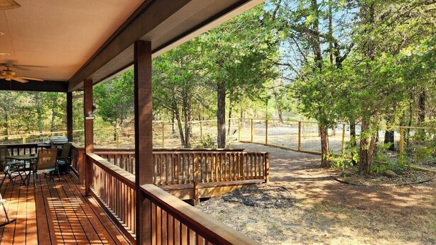 A wooden deck with a railing, a bench, and a table with chairs. - The Cottage, A Tranquil Pet-Friendly Retreat on 42 Acres at Lost Pines Shire (Paige)