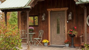 Eine rustikale Holzhütte mit Veranda, zwei Metallstühlen, einem kleinen Tisch und Blumentöpfen.