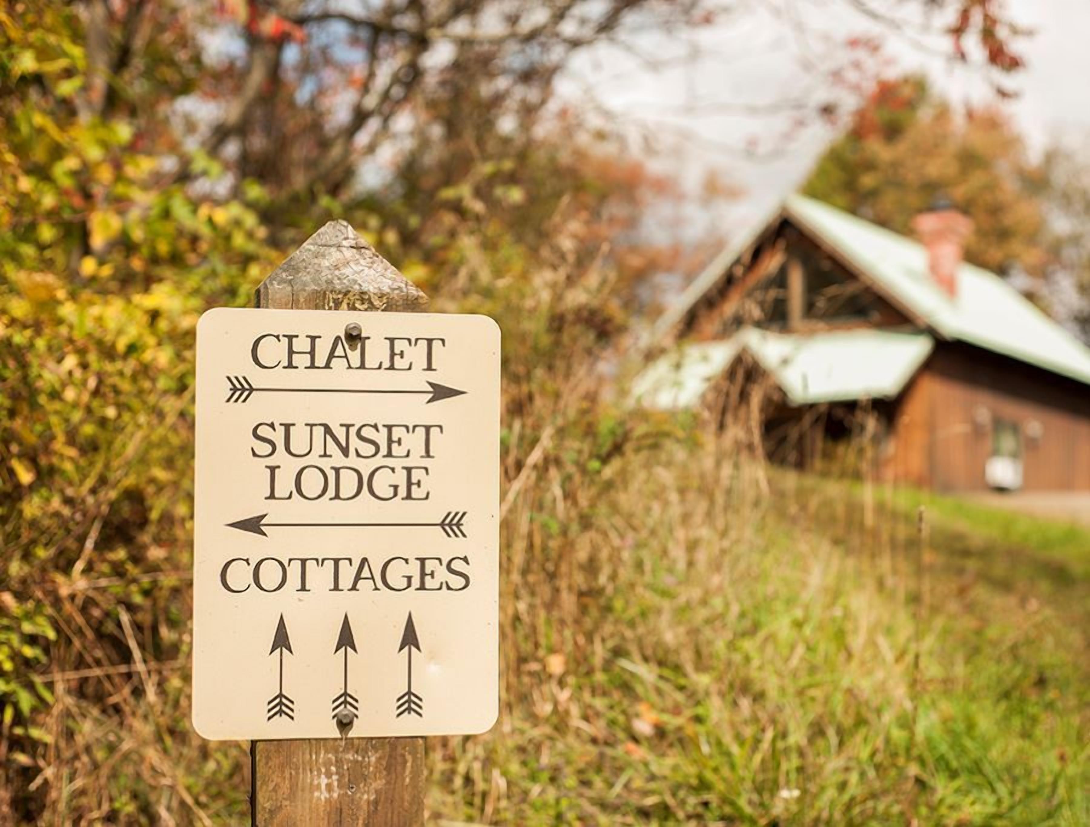 Panneau indicateur pour un chalet, un refuge avec vue sur le coucher de soleil et des maisons de vacances.