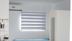 A modern bedroom with a bed, a sofa, a desk, and a window with blinds. - Villa Valentina Aruba (Noord)