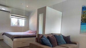 A bedroom with a bed, a sofa, a window, and an air conditioning unit. - Villa Valentina Aruba (Noord)