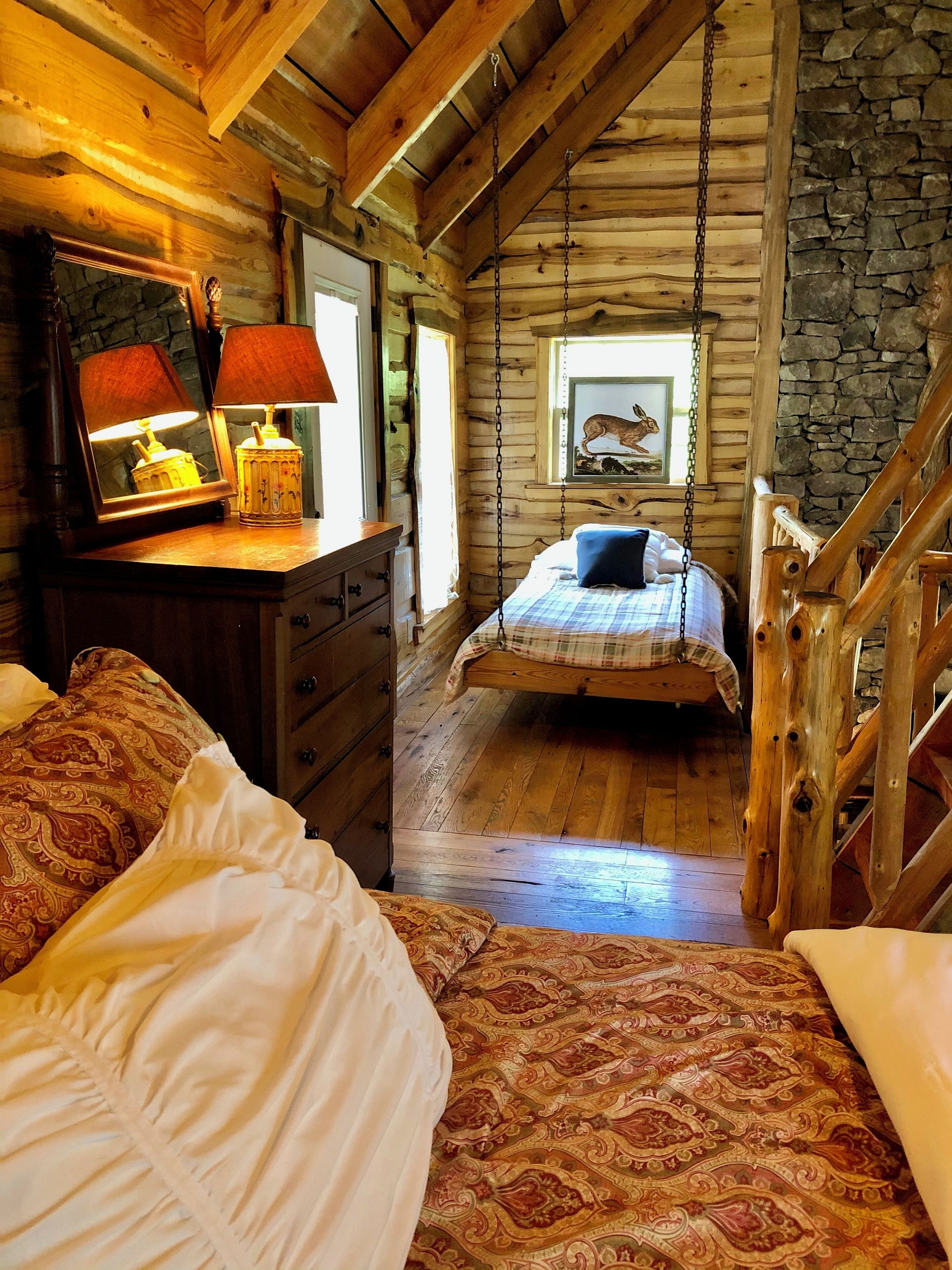 A cozy log cabin bedroom with a bed, a dresser, and a hanging chair.