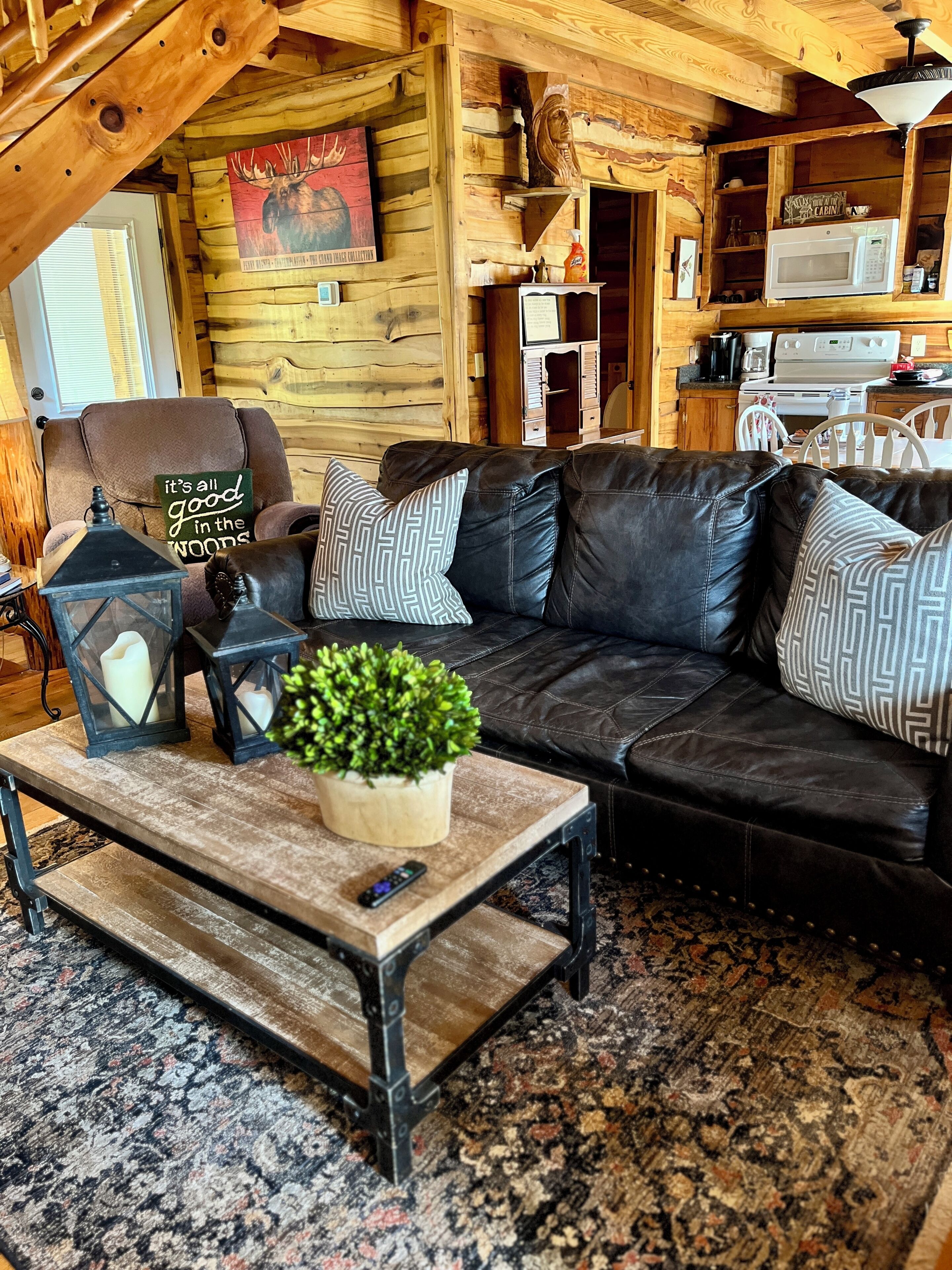 Een knus houten interieur met een leren bank, een houten salontafel en een landelijke keukenhoek.