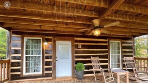 A log cabin with a wooden deck, a door with glass panels, and two wooden chairs.