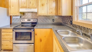 A kitchen with wooden cabinets, a stainless steel sink, and a window. - Pet-Friendly Cabin with Designated Boat Slip! (Greers Ferry)