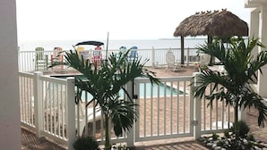 Ein Poolbereich mit Liegestühlen, einem Strohdachschirm und Blick auf das Meer.