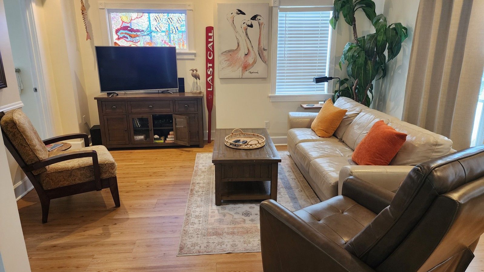 Una sala de estar con sofá, sillón, mesa de centro, televisor, estantería y ventana con persianas.