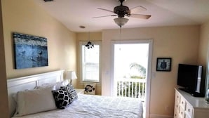 Ein Schlafzimmer mit einem Bett, einem Deckenventilator, einem Fernseher und einem Balkon mit Geländer.