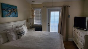 A bedroom with a bed, a television, a painting, and a window with curtains.