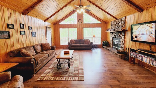 A cozy wooden interior with a high ceiling, a fireplace, a TV, and a bookshelf. - Cozy Cabin at Little River Canyon (Fort Payne)