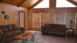 A wooden-paneled living room with two brown leather sofas, a wooden coffee table, and a patterned rug. - Cozy Cabin at Little River Canyon (Fort Payne)