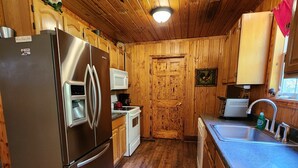 A kitchen with wooden walls, a stainless steel refrigerator, a microwave, a sink, and a wooden floor. - Cozy Cabin at Little River Canyon (Fort Payne)