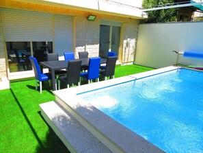 A swimming pool with a tiled deck, surrounded by a patio area with a table and chairs. - Private Heated Swimming Pool (Porto)