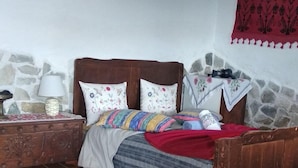 A bedroom with a wooden bed, a nightstand, a stone wall, and a painting. - Small Detached House Of 60 M2 Situated In Koukourava, Makrinitsa In Pelion Mt. (Μακρινίτσα, Κουκουράβα)