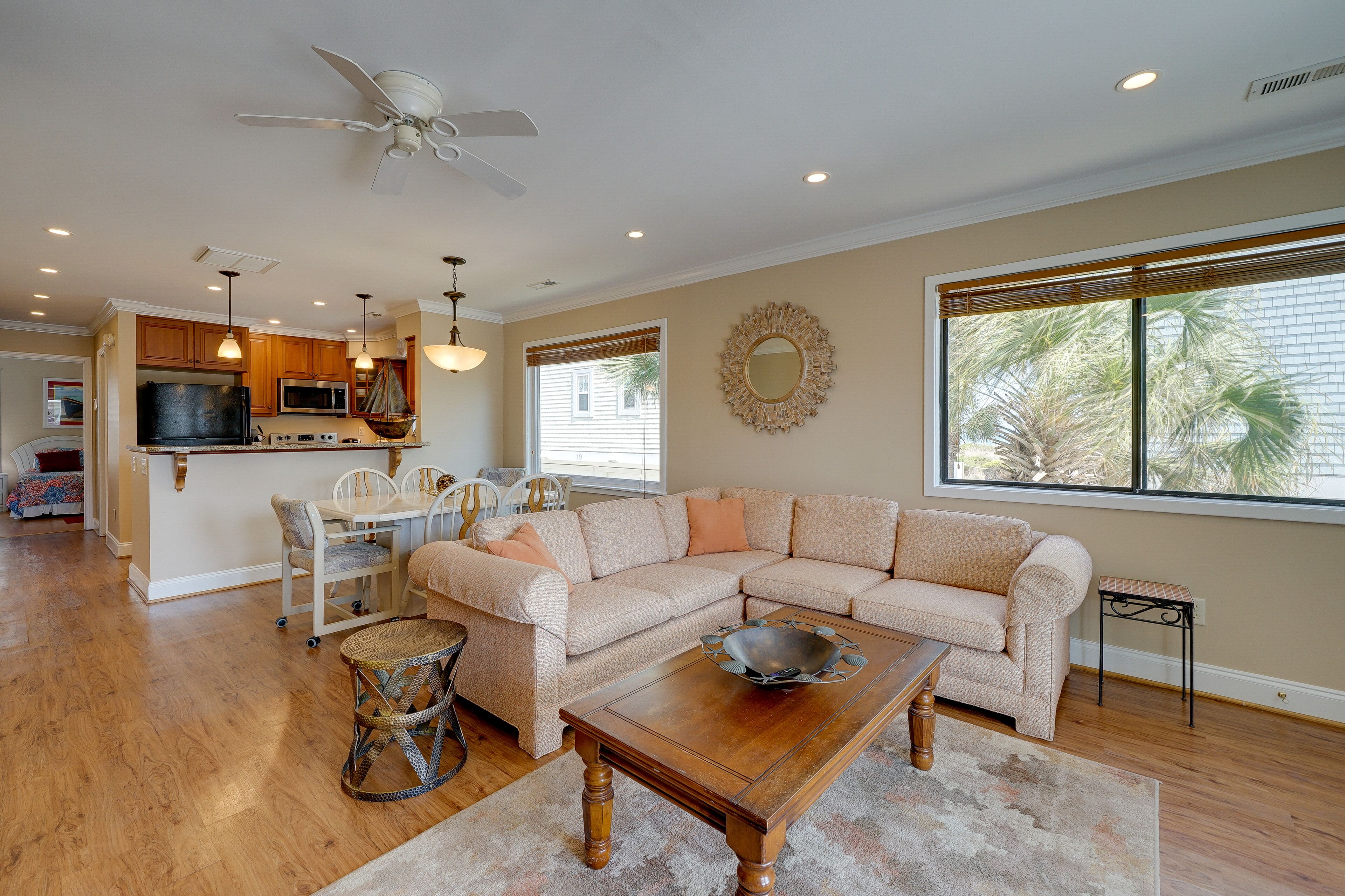 A spacious living room with a beige sectional sofa, a wooden coffee table, and a dining area with a white table and chairs.