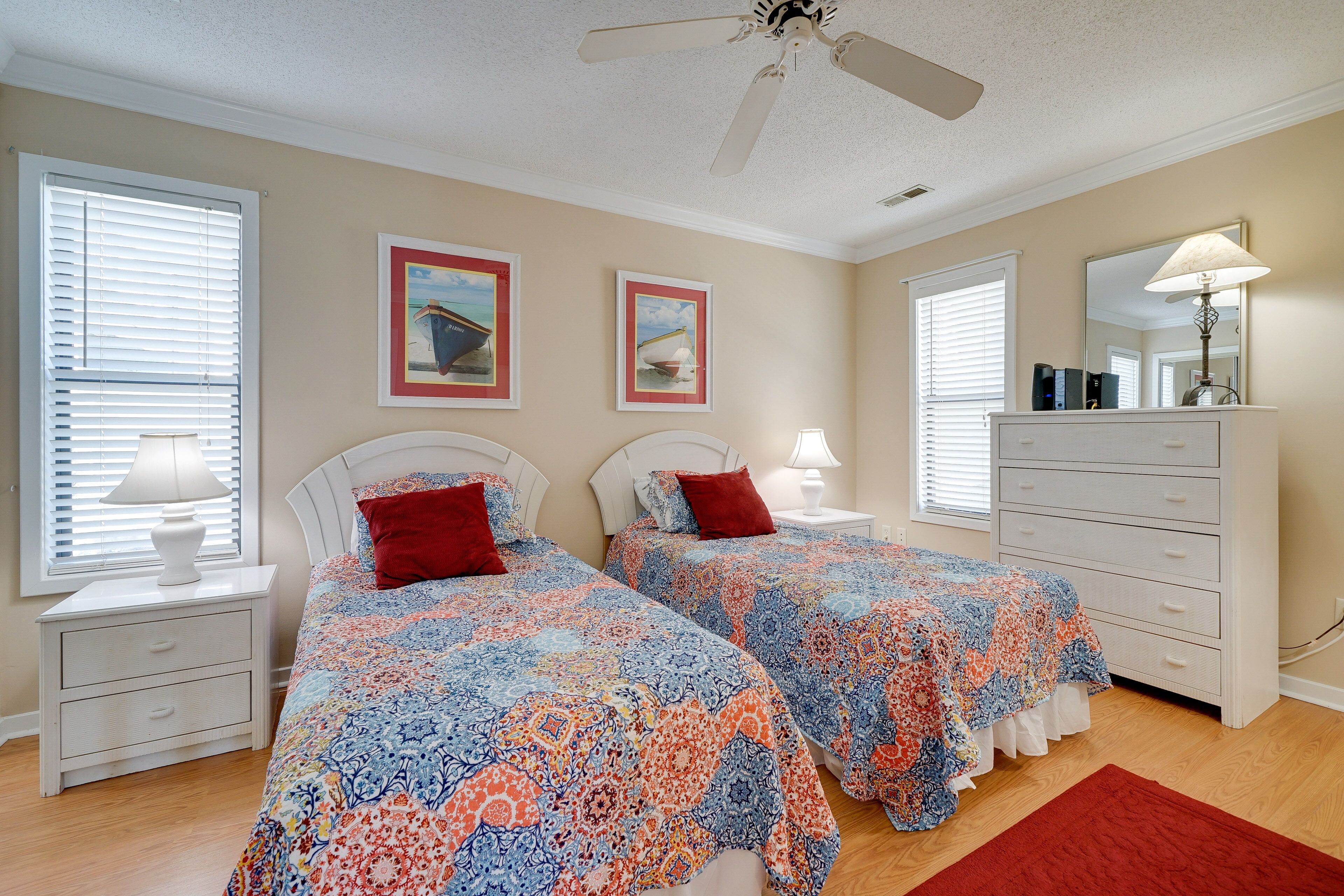 A bedroom with two beds, a dresser, a ceiling fan, and framed pictures on the wall.