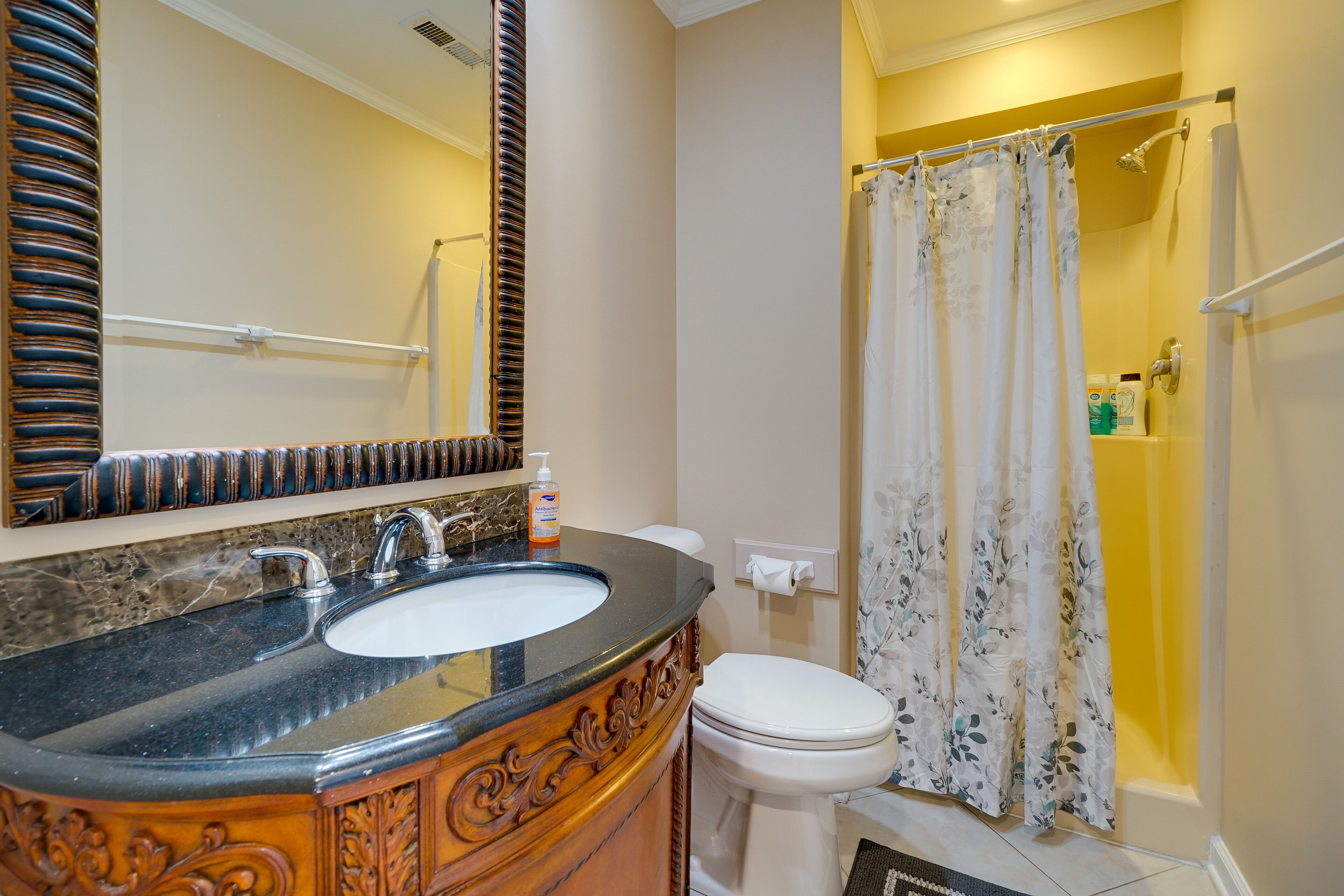 Ein Badezimmer mit Marmorwaschbecken, Holzwaschtisch, Toilette und Dusche mit Blumenmuster.
