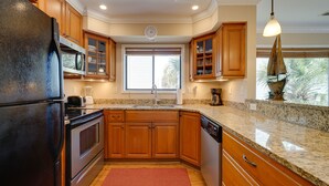 A kitchen with wooden cabinets, granite countertops, a refrigerator, a dishwasher, and a window with blinds.