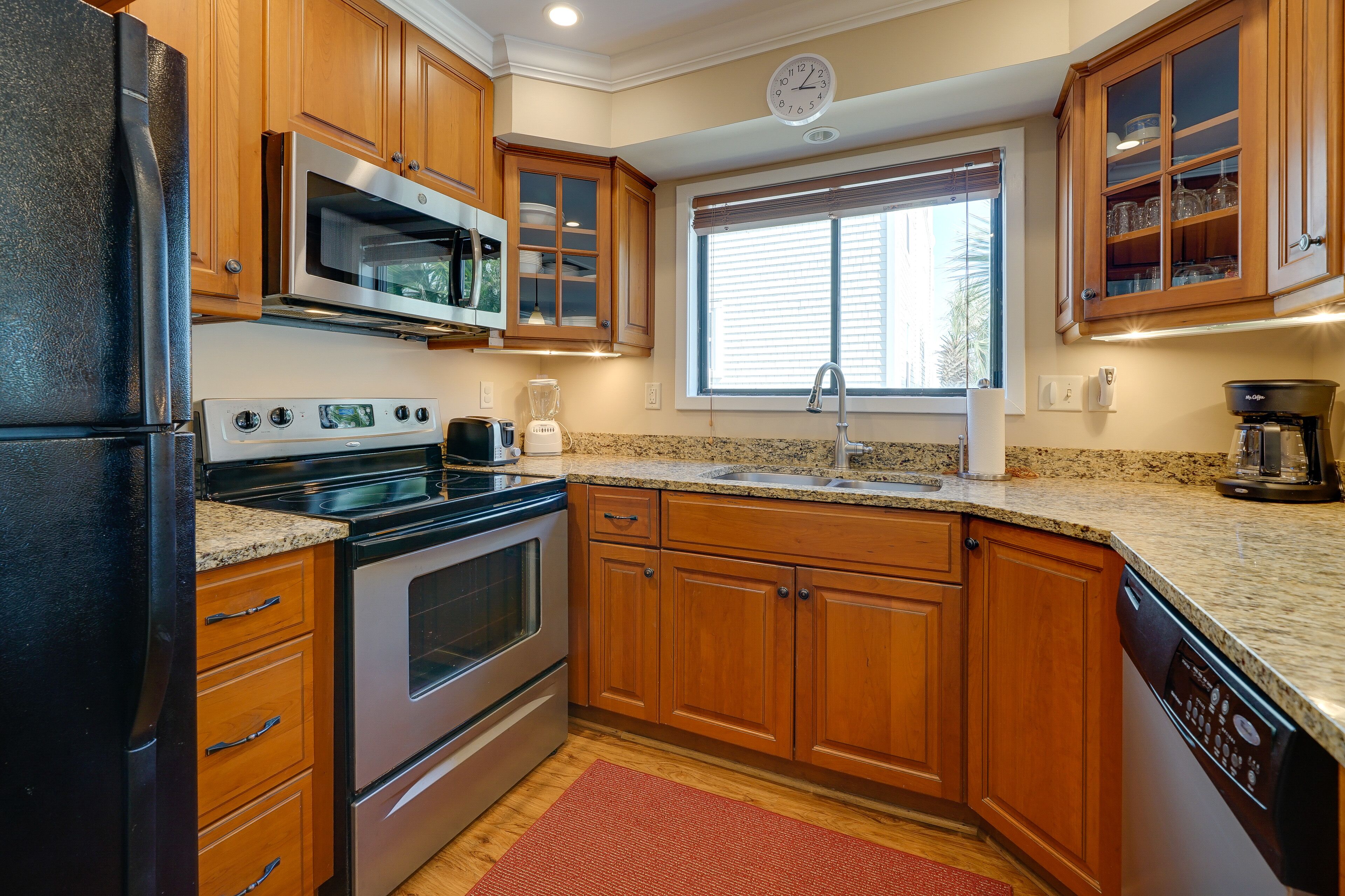 A kitchen with wooden cabinets, stainless steel appliances, a granite countertop, and a window with blinds.