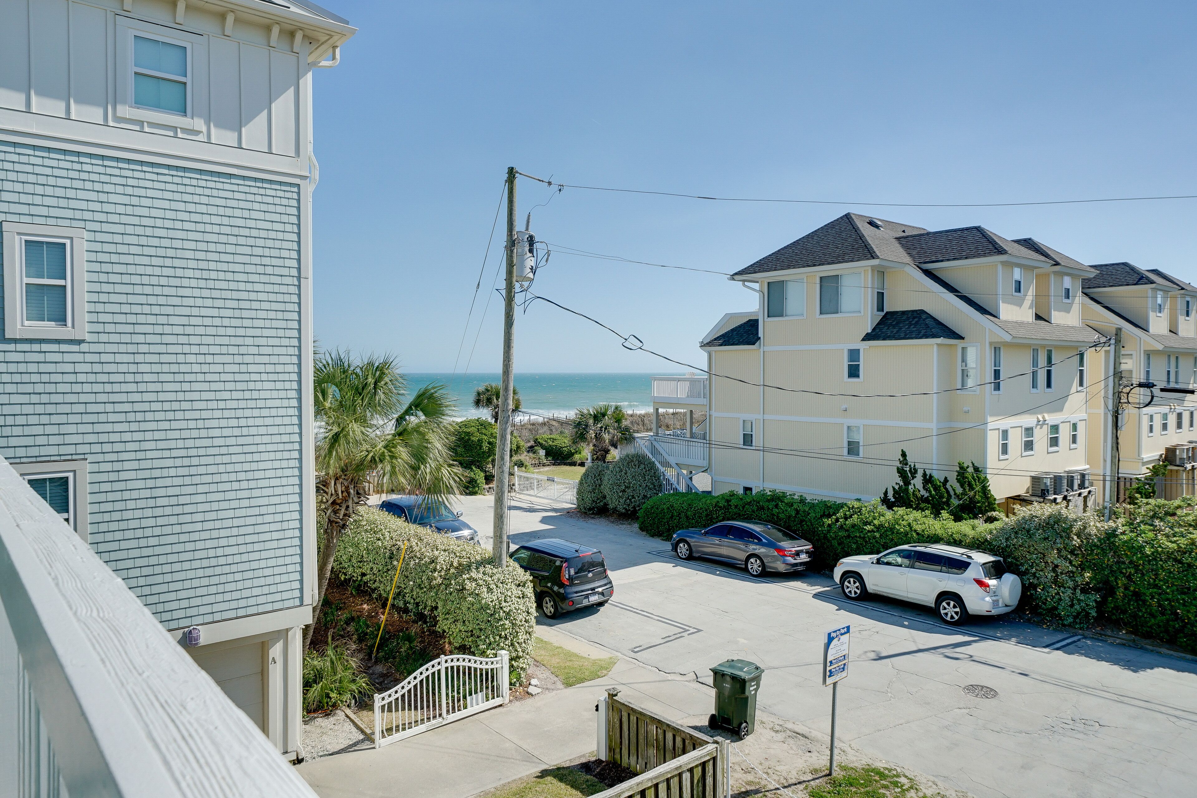 A coastal residential area with multi-story buildings, a parking lot, and a clear view of the ocean.