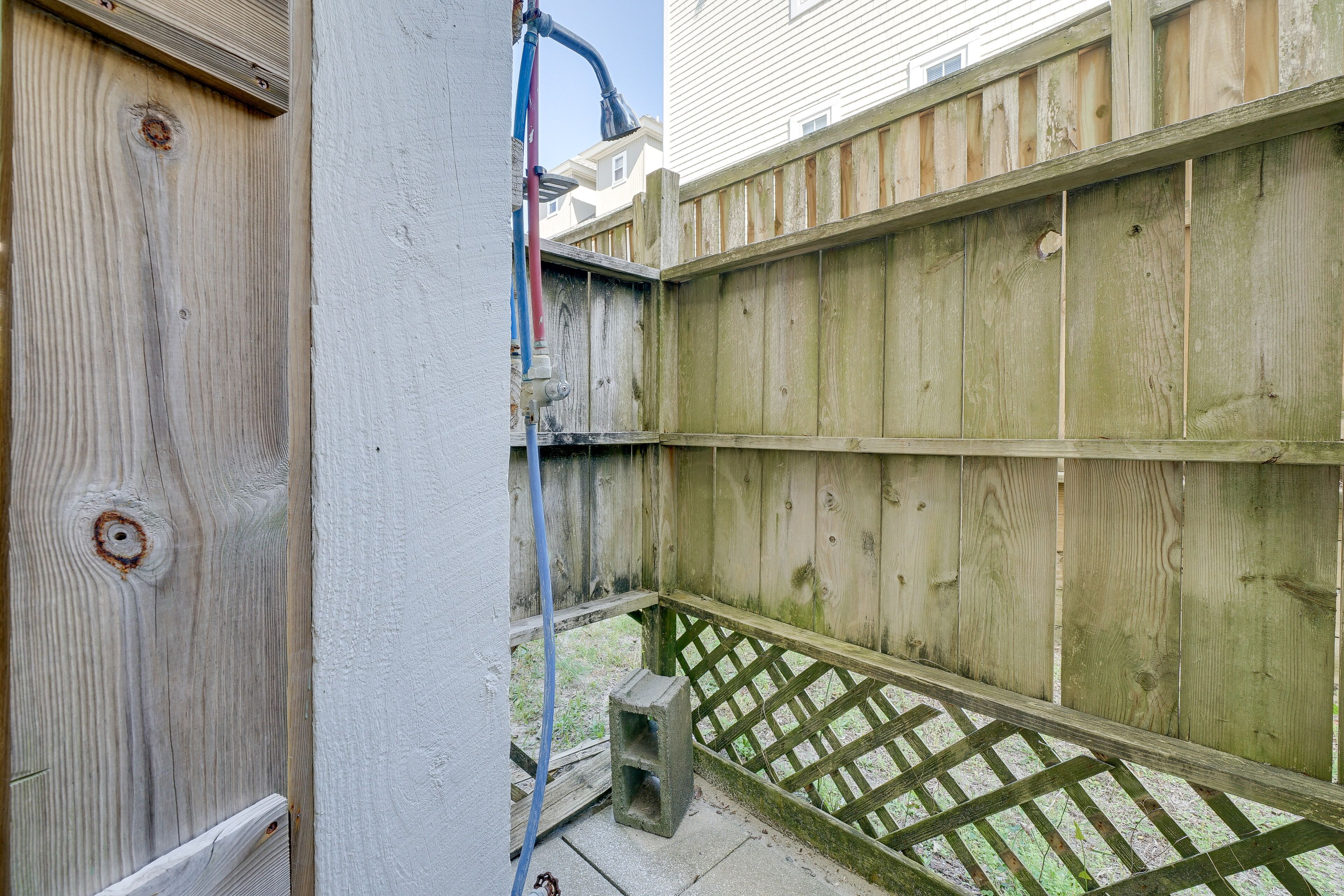 A wooden fence with a lattice bottom, a concrete block, and a blue hose.