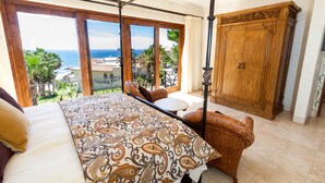 Une chambre avec un grand lit, une armoire en bois, un balcon avec vue sur l’océan et une table à manger.