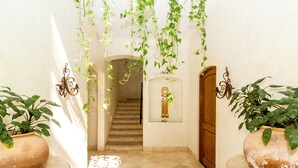 Un couloir avec un escalier, des plantes en pot et une statue.