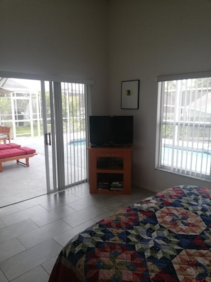 A room with a bed, a television on a wooden stand, and a sliding glass door leading to a patio with a pool. - Family Golf Resort 'Villa Bonita' Southern Dunes Florida (Haines City)